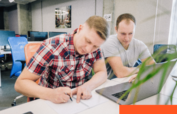 Two professionals collaborating around a laptop while taking notes